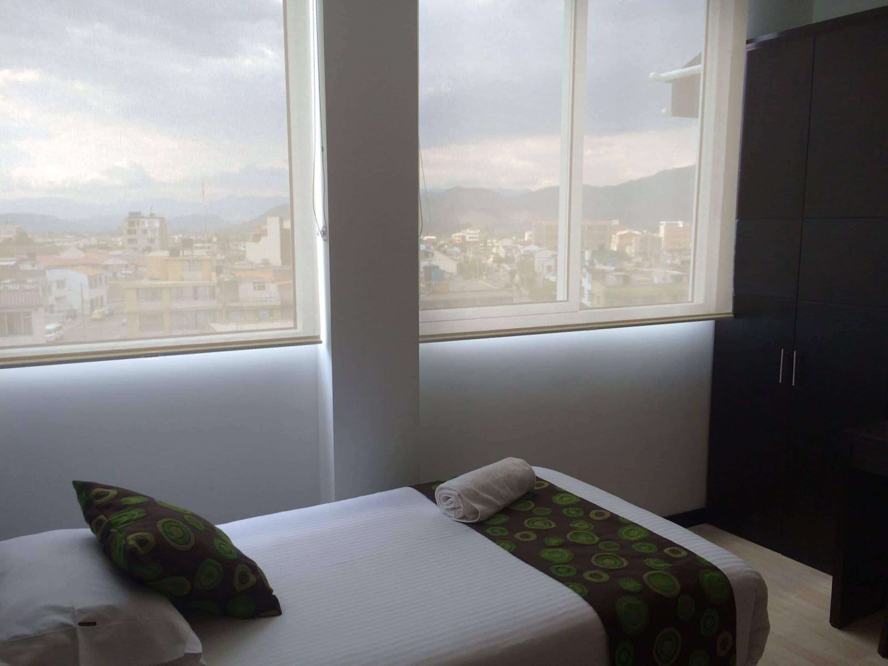 Una habitación de hotel con una cama, un ventanal con vista a la ciudad y un armario oscuro.