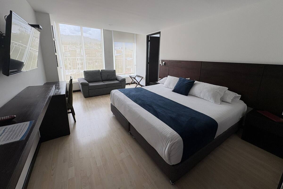 A modern hotel room with a large bed, a sofa, a desk, and a TV.