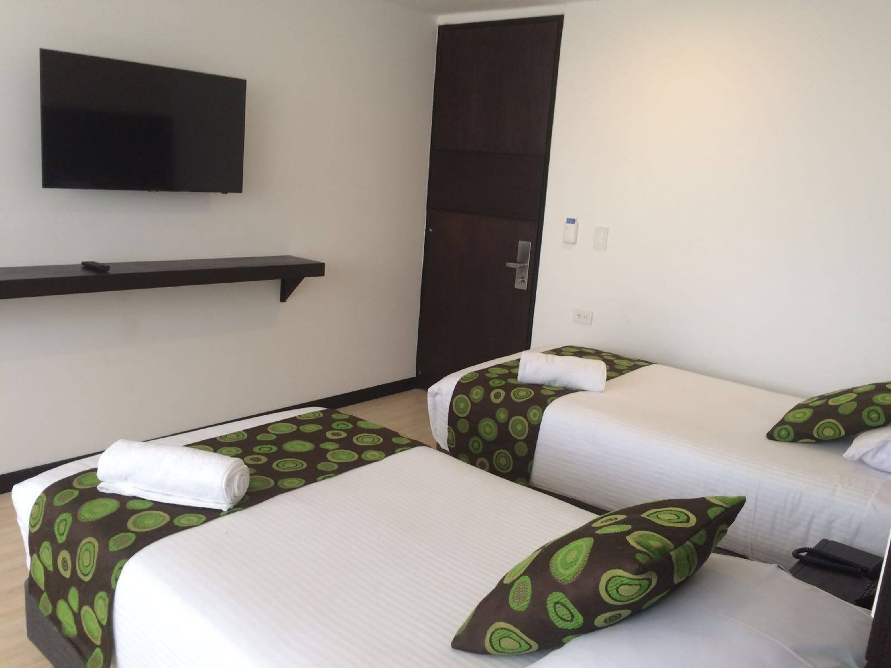 A hotel room with two beds, a TV mounted on the wall, and a door.