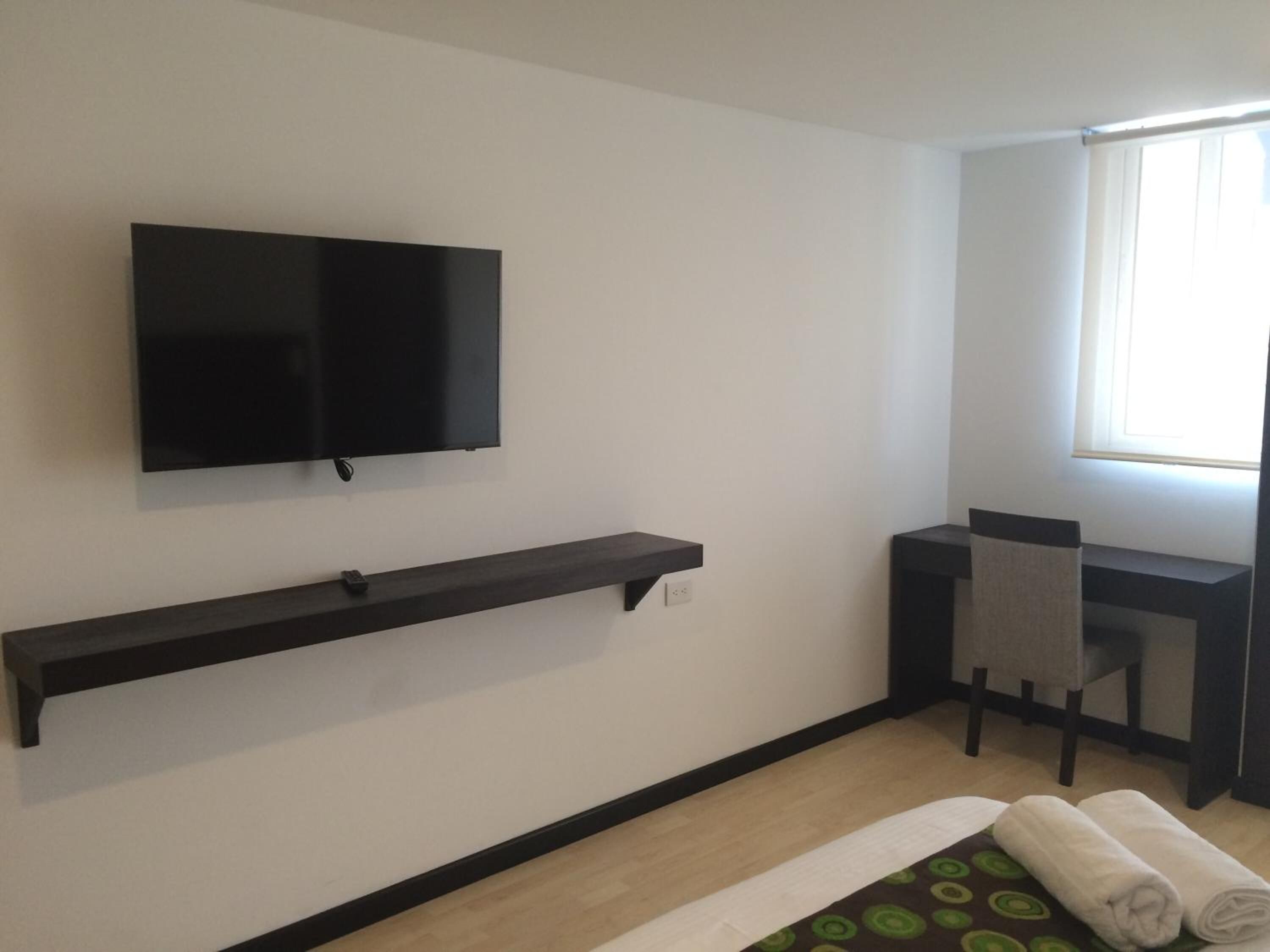 Une chambre d’hôtel équipée d’un téléviseur fixé au mur, d’un bureau avec une chaise, d’une fenêtre avec des rideaux et d’un lit recouvert d’une couvre-lit à motifs verts.