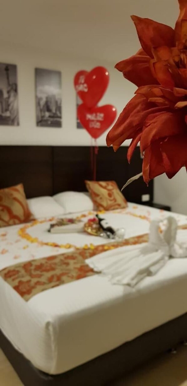 Una cama bien hecha con una colcha blanca, almohadas y un ramo de flores rojas.