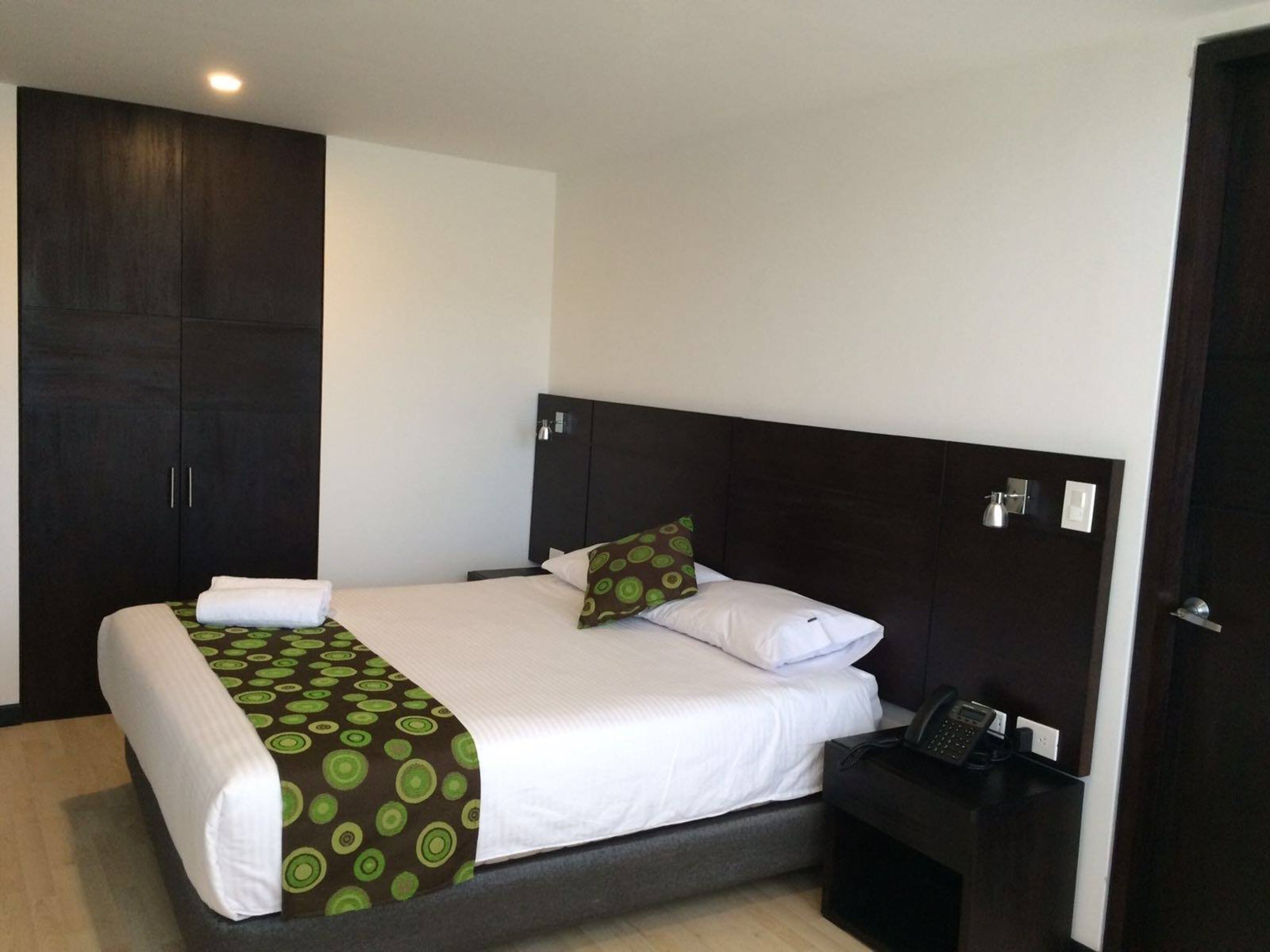 A hotel room with a bed, a bedside table with a phone, and a wardrobe.