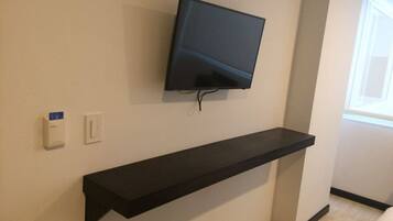 Una habitación moderna con un televisor montado en la pared, un estante negro debajo y un pequeño portaletras a la izquierda.