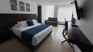 A modern hotel room with a large bed, a desk, and a view of the city.