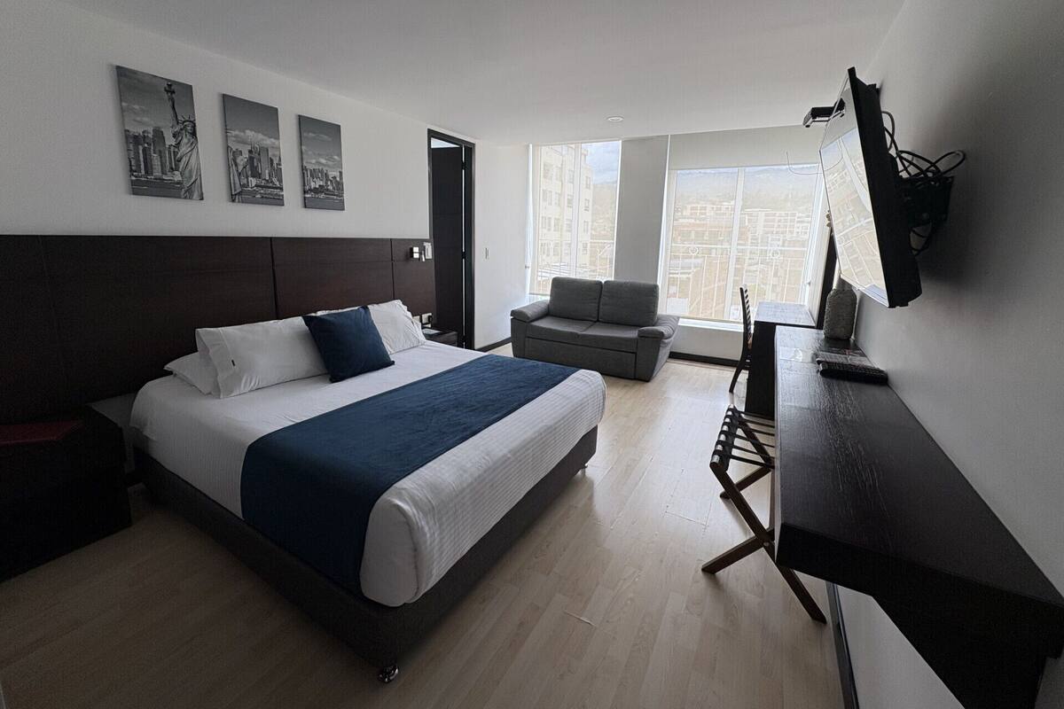 A modern hotel room with a large bed, a desk, and a view of the city.