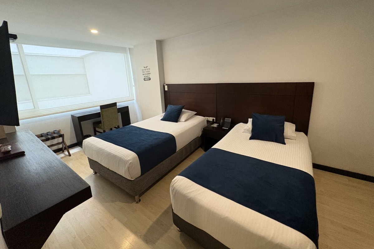 A hotel room with two beds, a desk, and a chair.