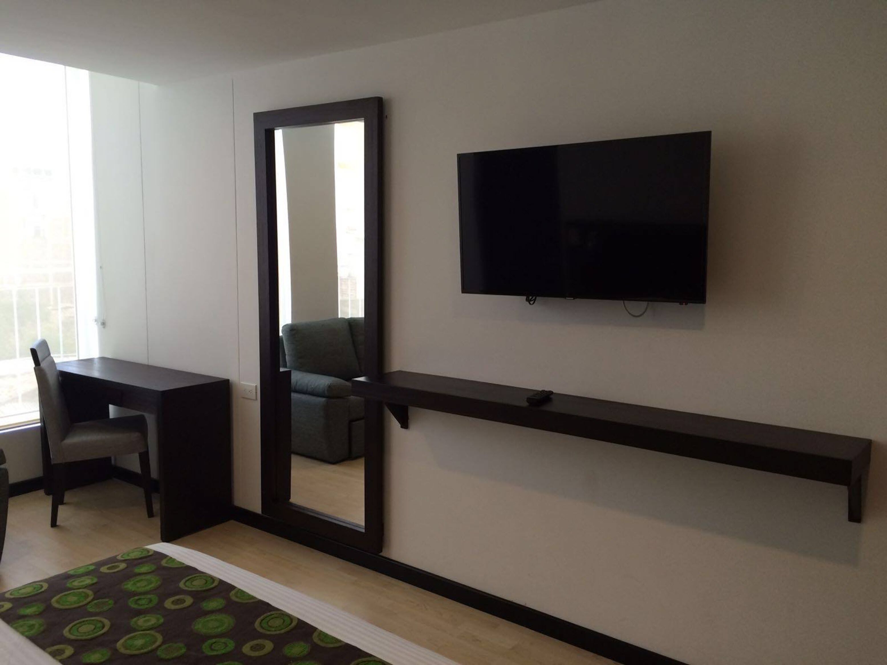 A modern room with a desk, chair, TV, and a mirror.