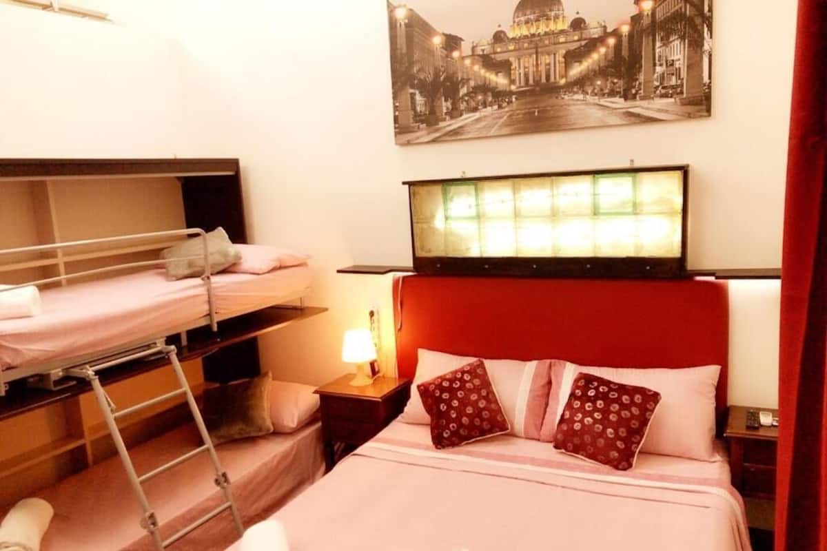A hotel room with bunk beds, a bed with a red headboard, a nightstand with a lamp, and a wall-mounted TV.