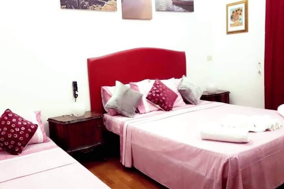 A bedroom with a red headboard, two beds, and a bedside table with a lamp.