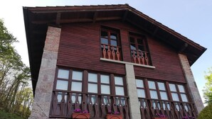 Un edificio de dos pisos con base de piedra y pisos superiores de madera. Cuenta con ventanas grandes, barandillas de madera decorativas y jardineras en la planta baja.