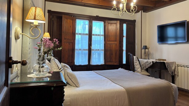 Un dormitorio con cama, lámpara de araña, televisor y ventana con cortinas.