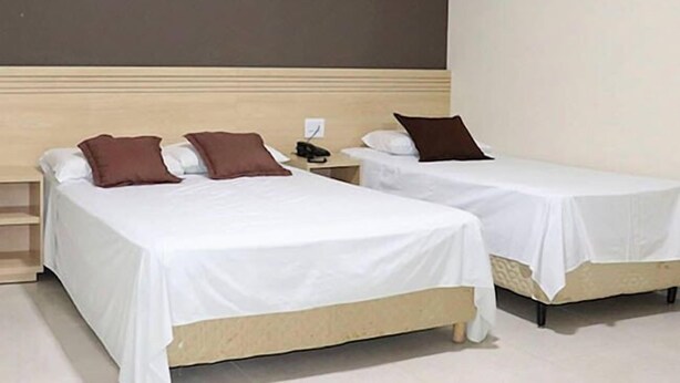 Two single beds with white linens and brown pillows, a wooden headboard, and a plain wall. - Tis Hotel 153 (Prata)