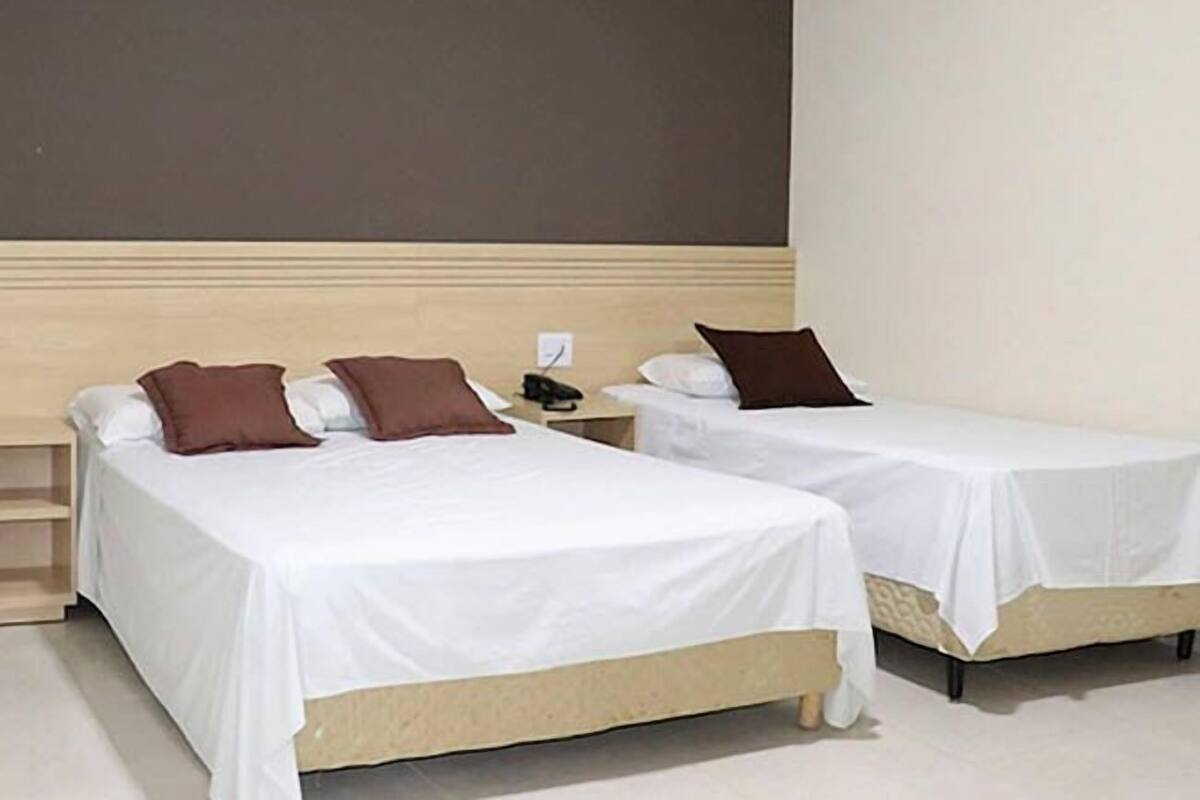 Two single beds with white linens and brown pillows, a wooden headboard, and a plain wall.