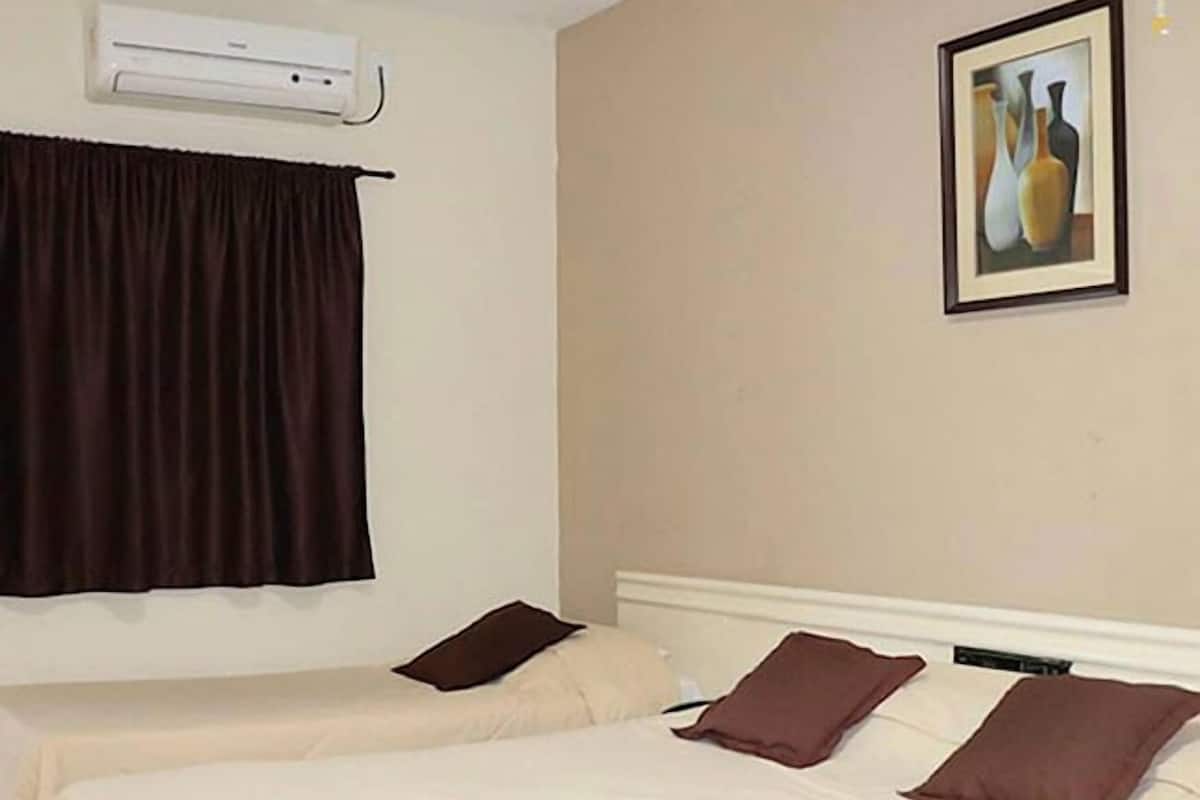 A hotel room with two beds, a painting on the wall, and an air conditioning unit.