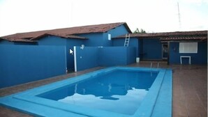 A swimming pool with a blue tiled deck, surrounded by a blue wall and a building with a red roof. - Tis Hotel 153 (Prata)