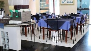 A dining area with tables and chairs, a counter with a cash register, and a refrigerator. - Tis Hotel 153 (Prata)