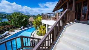 A pool area with a staircase leading to a balcony overlooking a body of water and lush greenery.