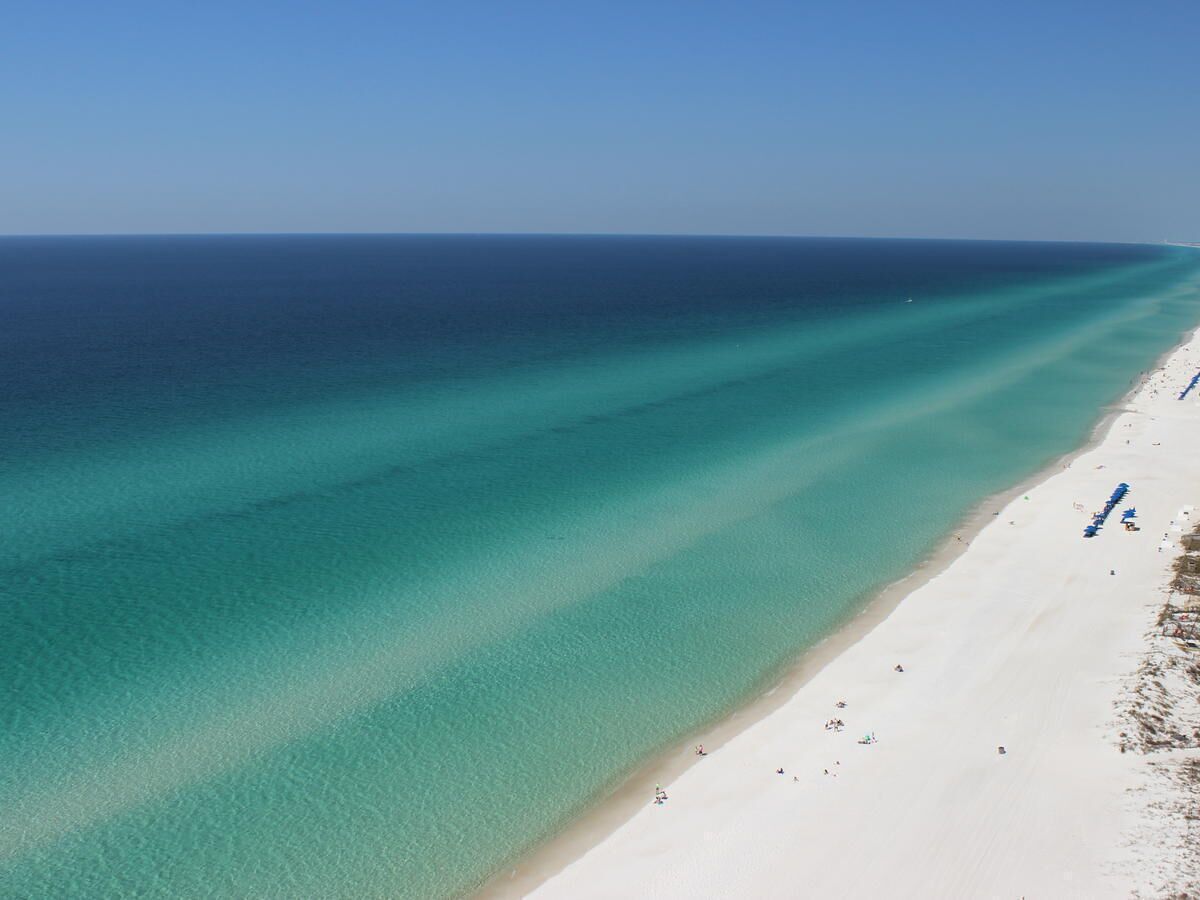 Une plage aux eaux turquoise et limpides, bordée d’un rivage sablonneux.