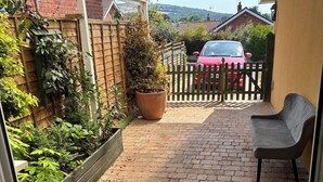 Eine Terrasse mit Backsteinpflasterung, einem Holzzaun, einem Blumentopf und einer Bank.