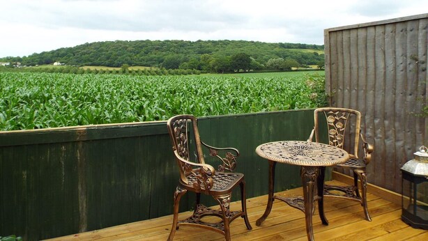 Eine Terrasse mit zwei verzierten Stühlen und einem Tisch, mit Blick auf ein grünes Feld und eine Hügelkuppe.