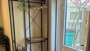 Ein Zimmer mit einer schwarzen Metallregaleinheit, einem kleinen Holztisch und Blick auf einen Baum durch ein Fenster.