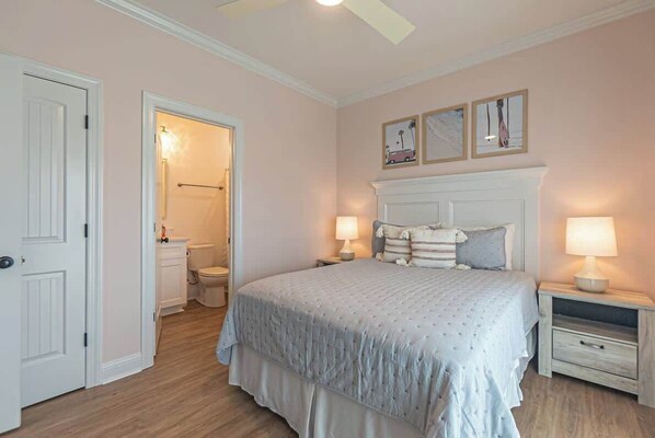 A bedroom with a bed, bedside tables, a nightstand, a door, and a bathroom visible through an open door. - Beach Please (Ocean Isle Beach)