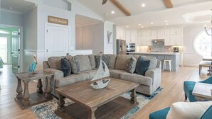 A spacious living room with a large sofa, a wooden coffee table, and a ceiling fan. - Beach Please (Ocean Isle Beach)