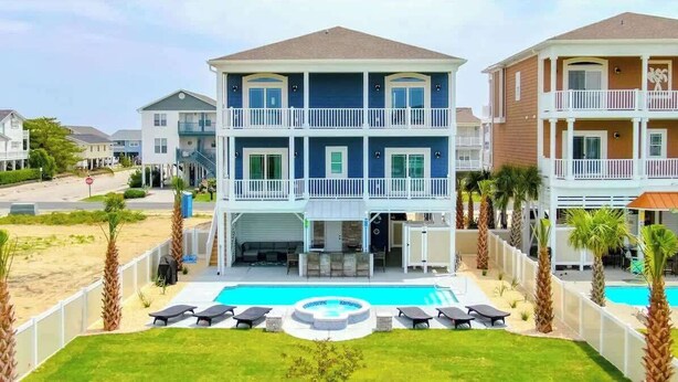 A multi-story hotel with a pool, outdoor seating, and a view of the beach. - Beach Please (Ocean Isle Beach)