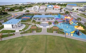 A playground with slides and climbing structures, surrounded by a parking area and a building with a blue roof.