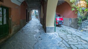 Un stretto vicolo con un'auto rossa parcheggiata sotto un arco, che conduce a un edificio con un cartello che recita "LEBERG AMICI".