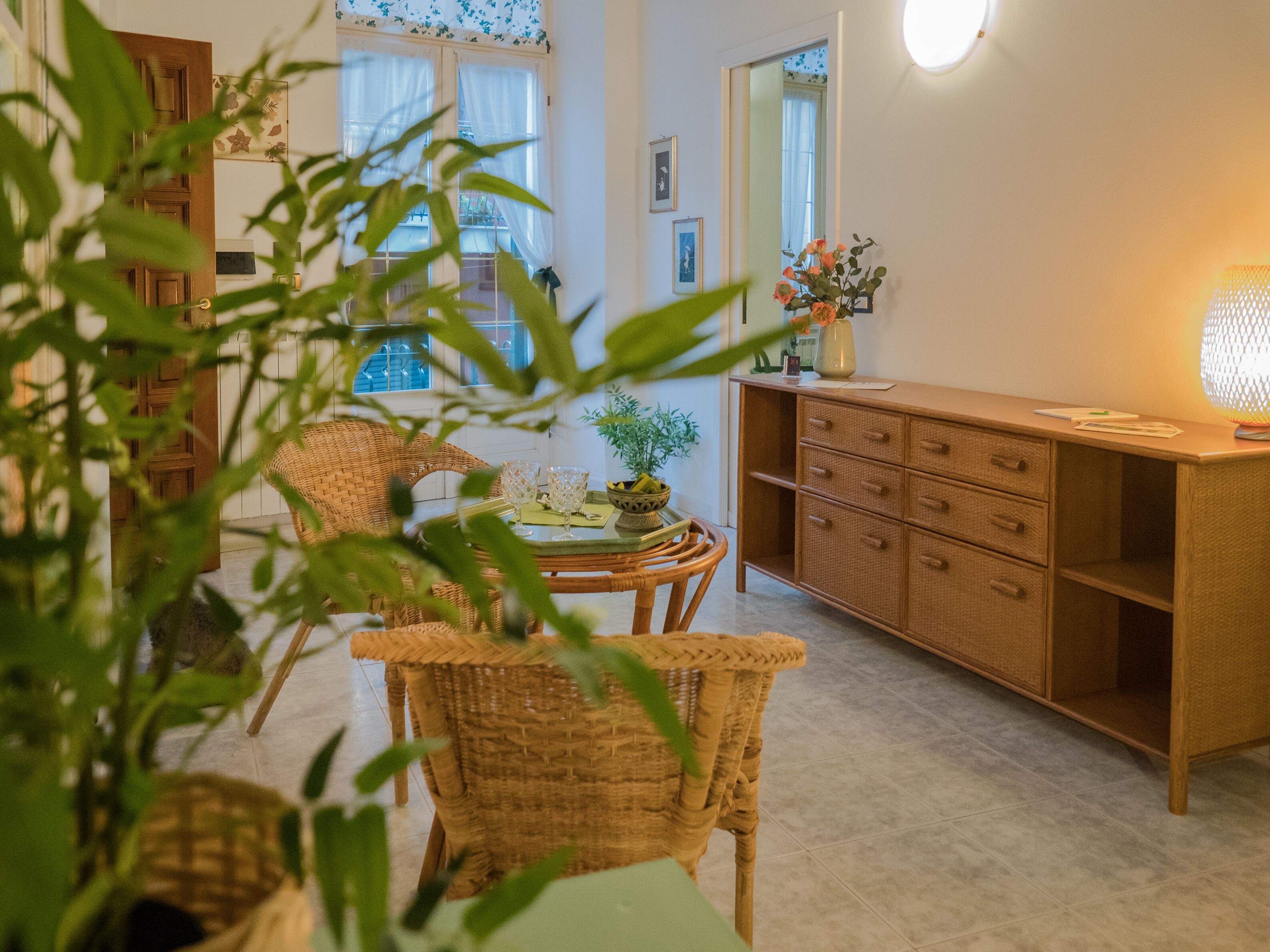 A room with a wicker chair, a wooden cabinet, and a table with a vase of flowers.