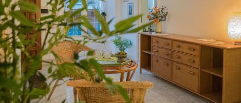 A room with a wicker chair, a wooden cabinet, and a table with a vase of flowers.
