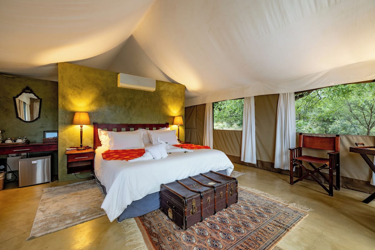 A spacious bedroom with a large bed, bedside lamps, a wooden chair, and a desk.