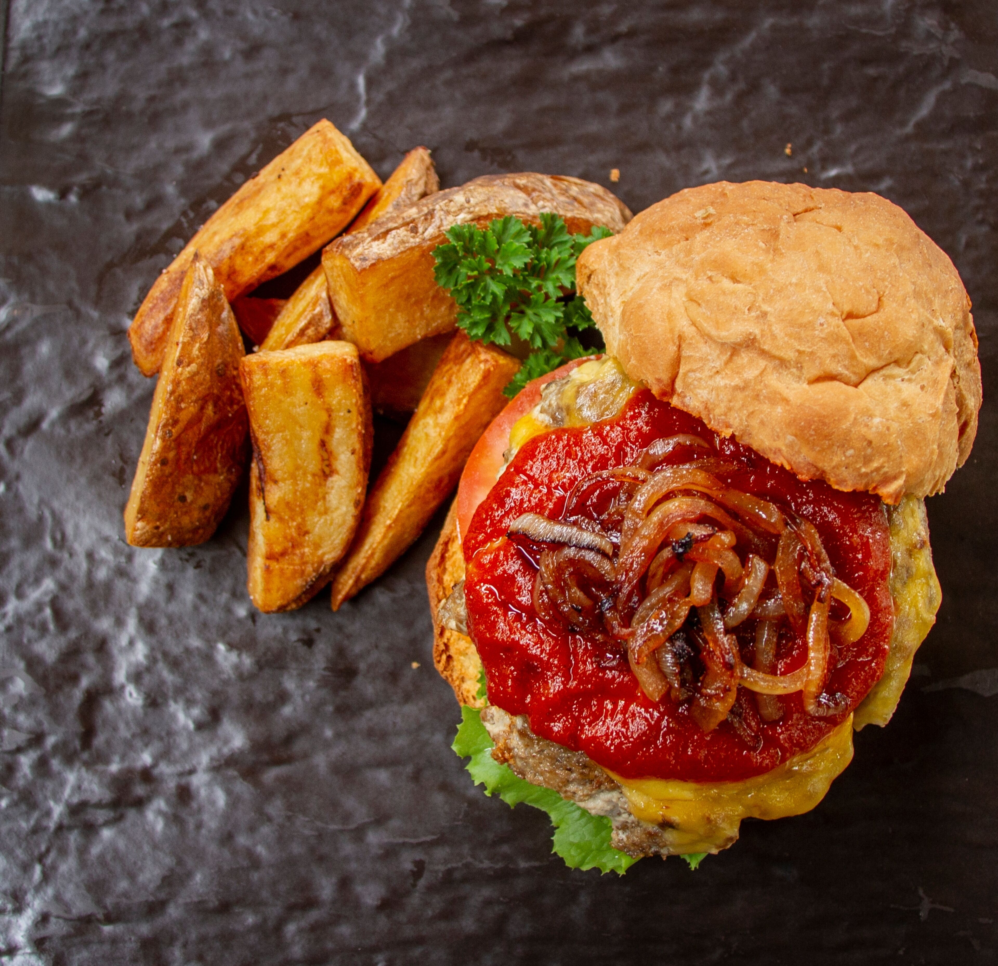 A sandwich with a bun, lettuce, tomato, and onions on a dark surface.