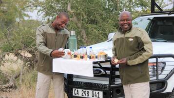 Two men standing by a table with food and drinks, in front of a vehicle with a license plate CA 298 041.