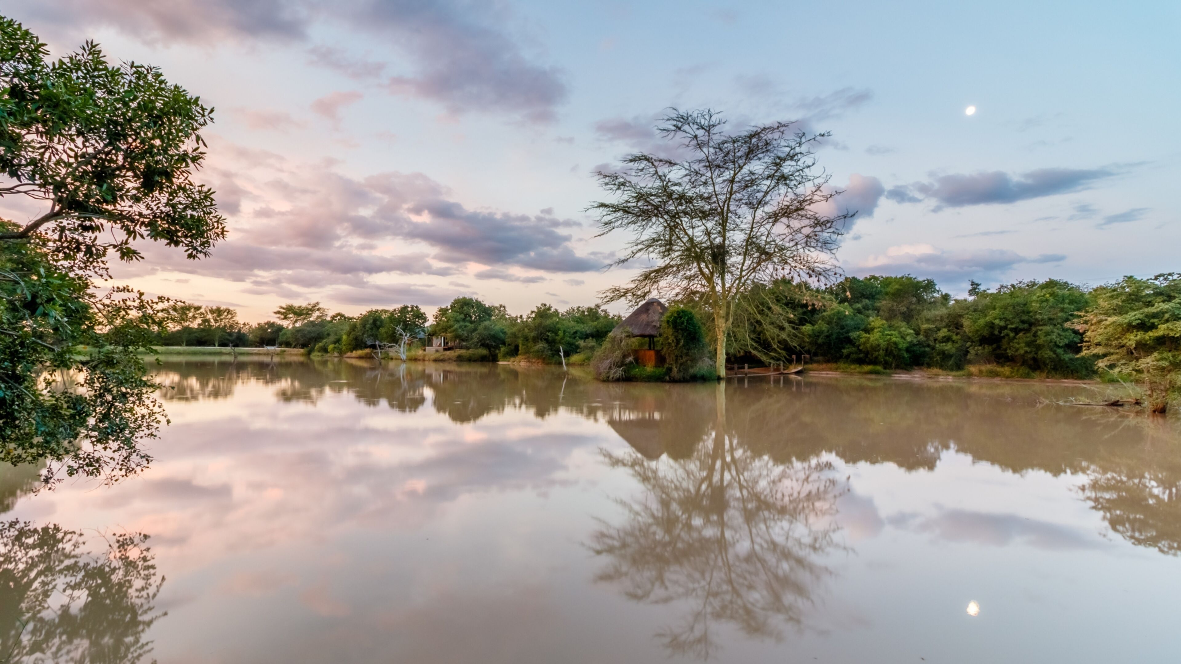 A serene lakeside scene with a thatched-roof hut and lush greenery.