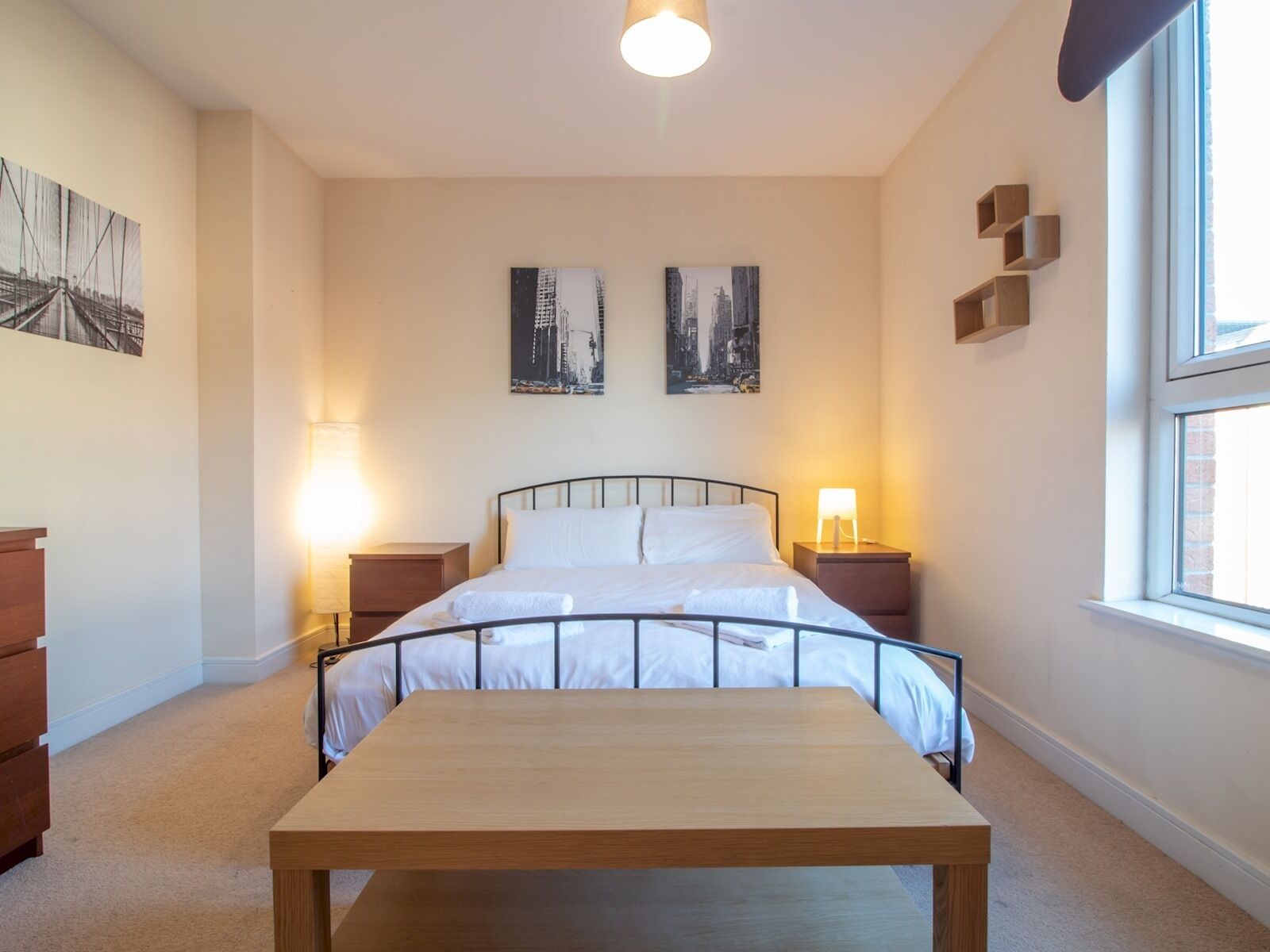 A bedroom with a bed, bedside tables, a wooden bench, and artwork on the walls.