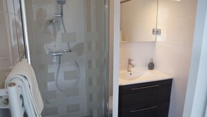 A modern bathroom with a glass-enclosed shower, a white sink, and dark-toned cabinets. - STUDIO DOWNTOWN LA BAULE (La Baule)