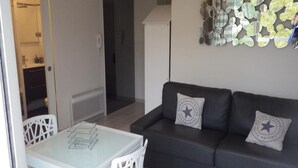 A modern living area with a glass-top dining table, white chairs, a dark leather sofa with star-patterned cushions, and a wall-mounted mirror art piece. - STUDIO DOWNTOWN LA BAULE (La Baule)