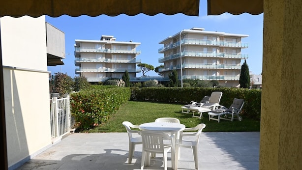 A patio with a table and chairs, a hedge, and two multi-story buildings in the background. - M251 - Marcelli, three-room apartment with garden 100m from the sea (Marcelli)