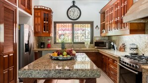 Una cocina con gabinetes de madera, encimera de granito, refrigerador de acero inoxidable, microondas y estufa.