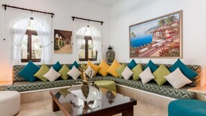 Una sala de estar con un sofá estampado, una mesa de centro y un cuadro que muestra una escena costera.