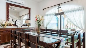 Un comedor con una mesa de vidrio, sillas acolchadas, un mueble de madera y un espejo grande.
