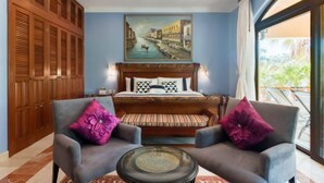 Un dormitorio con una cama, dos sillones, una mesa de centro de vidrio, un cuadro y vistas al exterior.