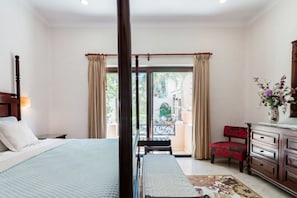 Une chambre à coucher comprenant un lit, une table de chevet, une commode, une chaise et un balcon avec des rideaux.