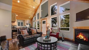 Ein gemütliches Wohnzimmer mit Kamin, Ledersofas, einem Couchtisch und großen Fenstern mit Blick ins Freie.