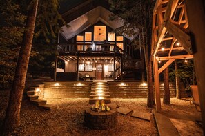 A wooden cabin with a balcony, a fire pit, and a staircase leading to the entrance.