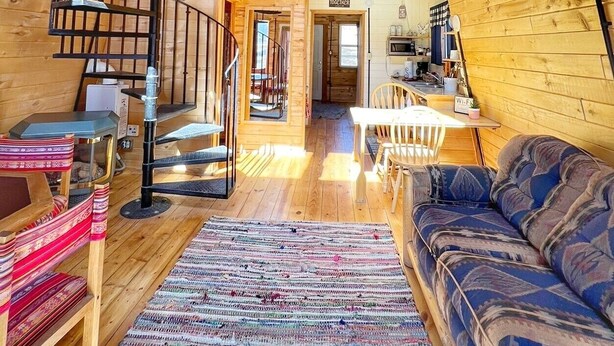 L’intérieur d’un chalet en bois comprend un escalier en colimaçon, un coin repas et un canapé.