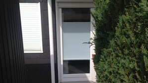 Una entrada residencial con una puerta cerrada, una ventana con persianas y un pequeño escalón que lleva a la puerta.