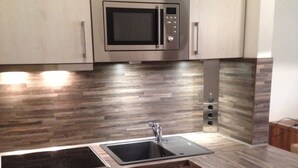 Una cocina moderna con microondas integrado, pileta de acero inoxidable y piso de madera.